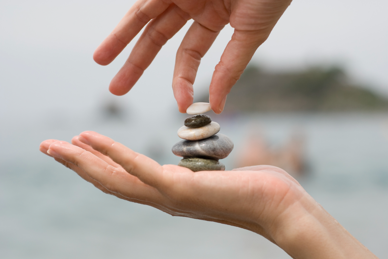 Hand stacking smooth stones by the beach.
