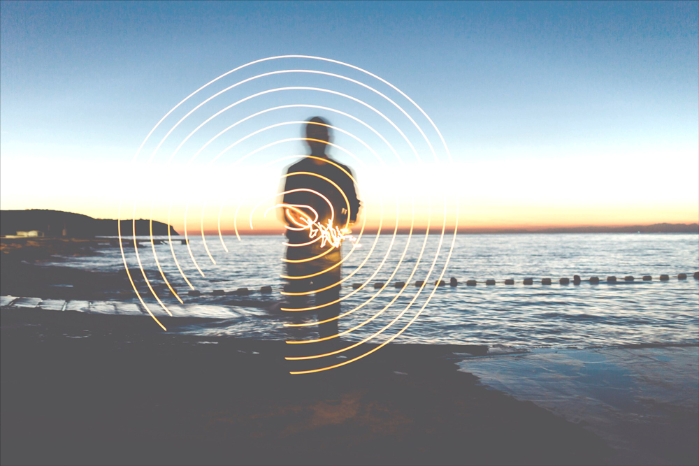 Person creating light patterns in front of ocean at sunset.