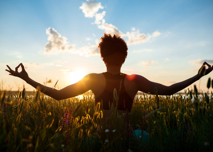 Person sitting in grass, meditating at sunrise.